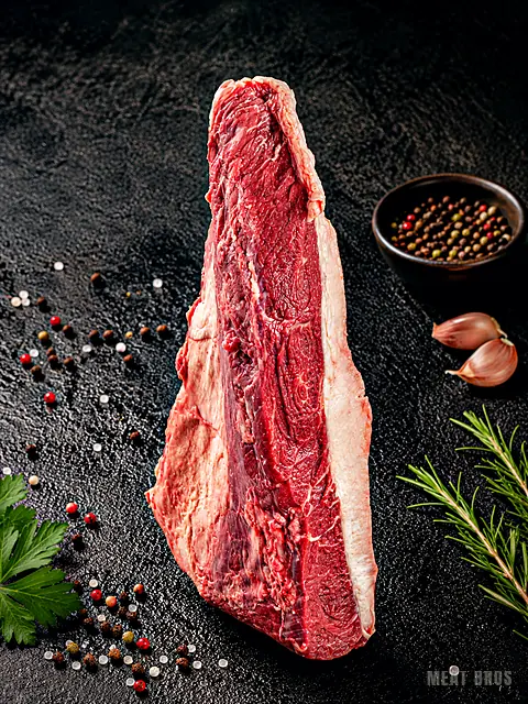Pieza larga de res con borde de grasa, junto a pimienta en grano